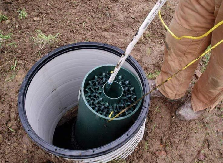 Person installing a well with a green cylinder in a cylindrical opening.