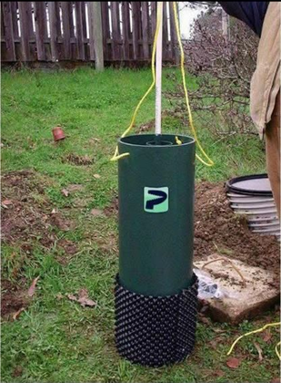 Green well casing with a black base and yellow ropes in a grassy yard.