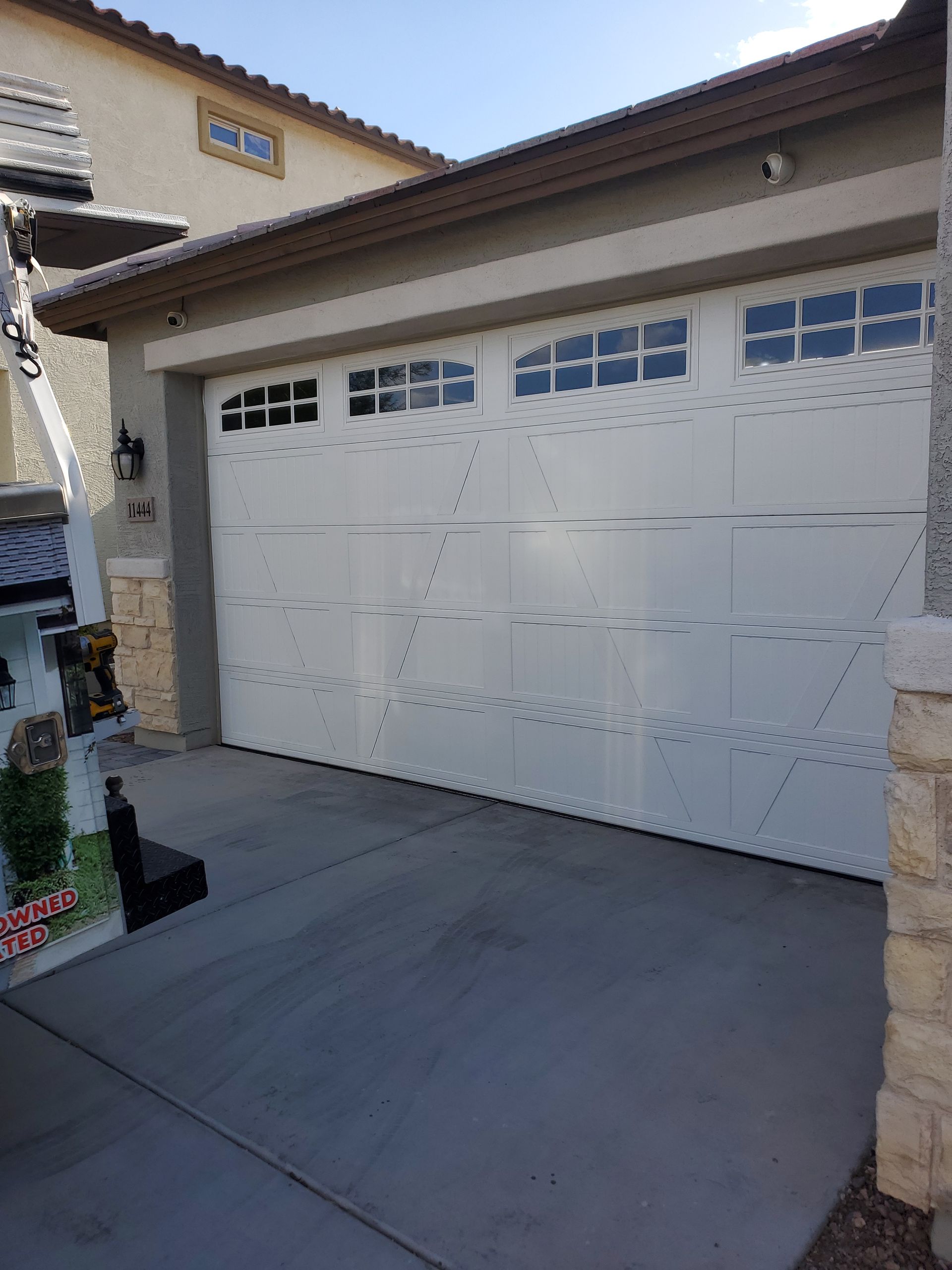 New White two-car garage door beside a beige house, viewed from a driveway in daylight