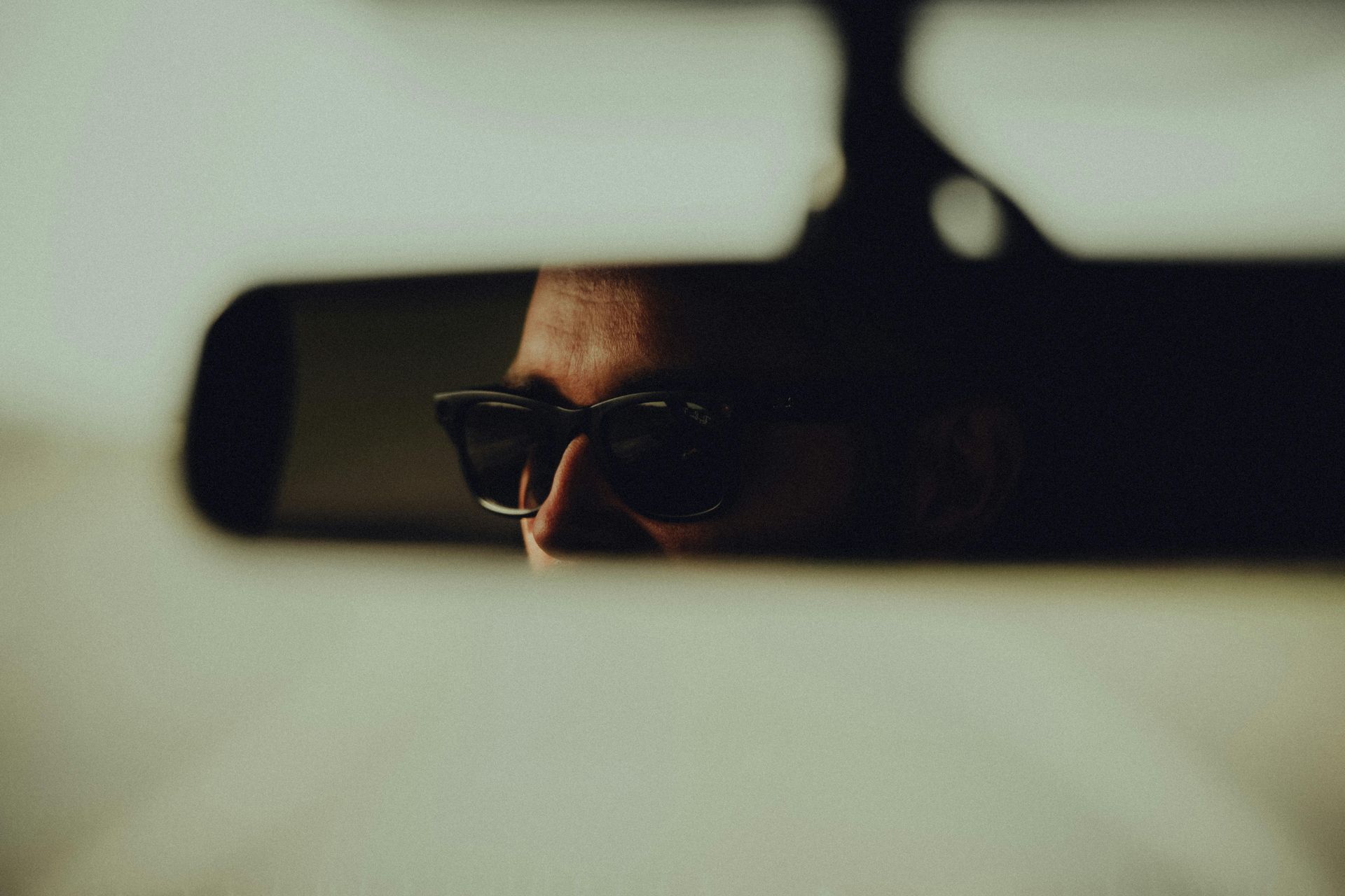 A man wearing sunglasses is looking at himself in the rear view mirror of a car.