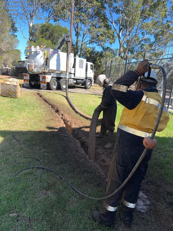 A man in a yellow shirt is holding a hose in front of a vacuum truck.