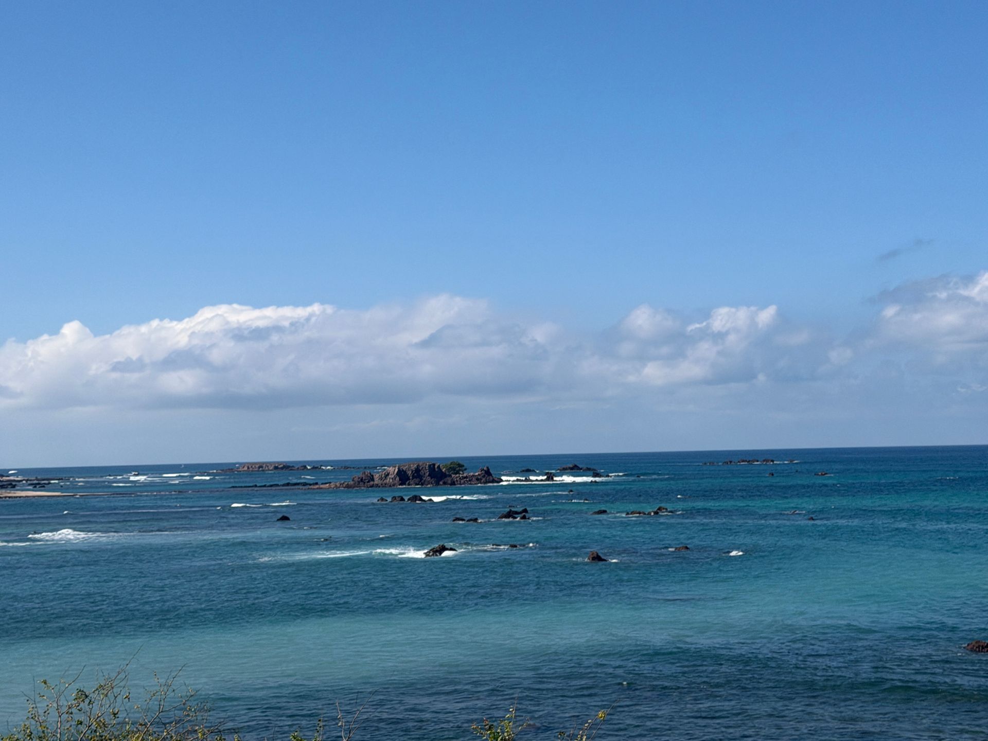 Calm blue ocean with rocky reef under a clear sky and distant clouds