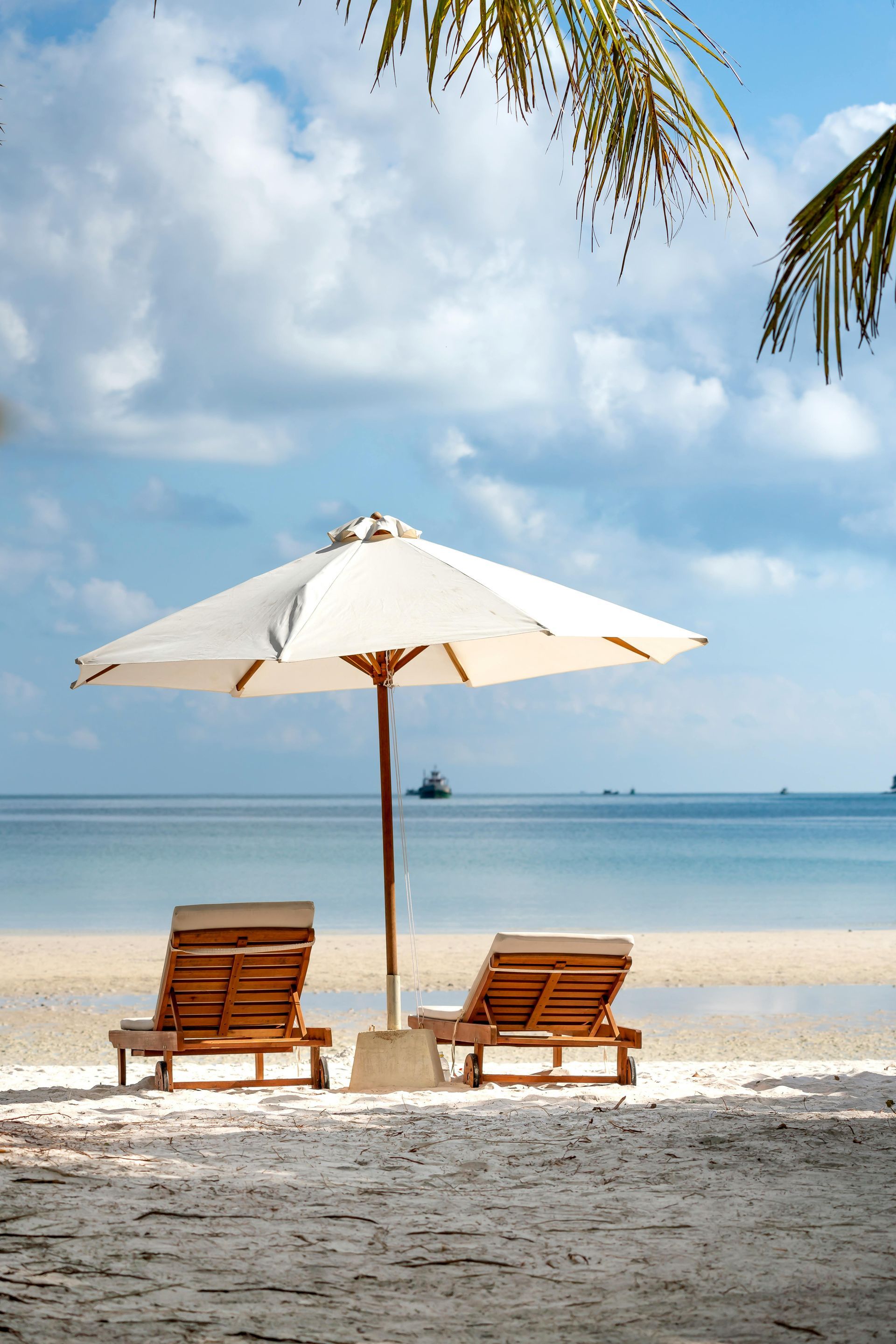 Two wooden beach chairs under a white umbrella on a sandy beach by calm blue sea