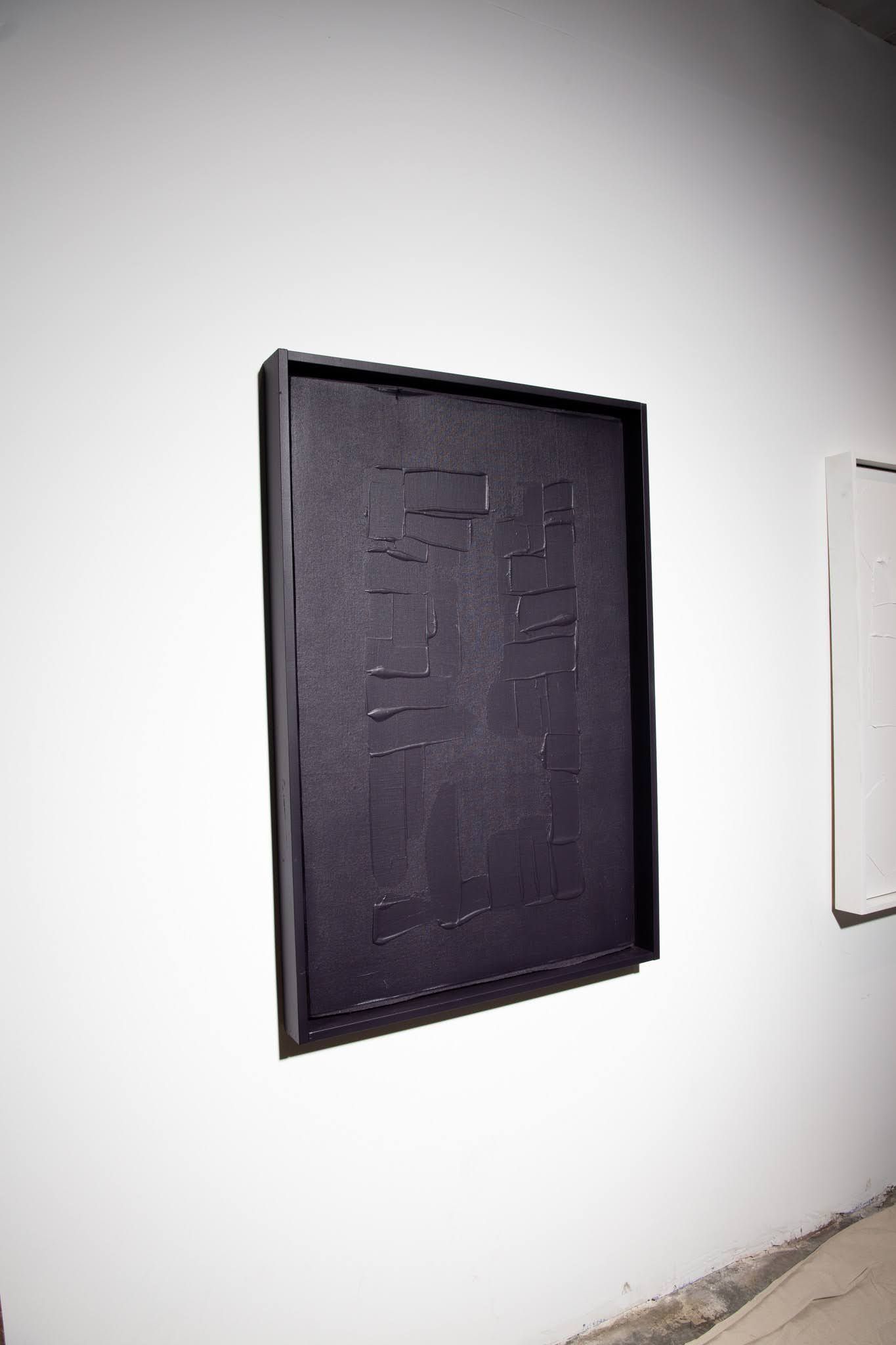Black framed artwork on a white wall. The artwork is a dark rectangle, possibly textured; art by Matt Remsbecher. 