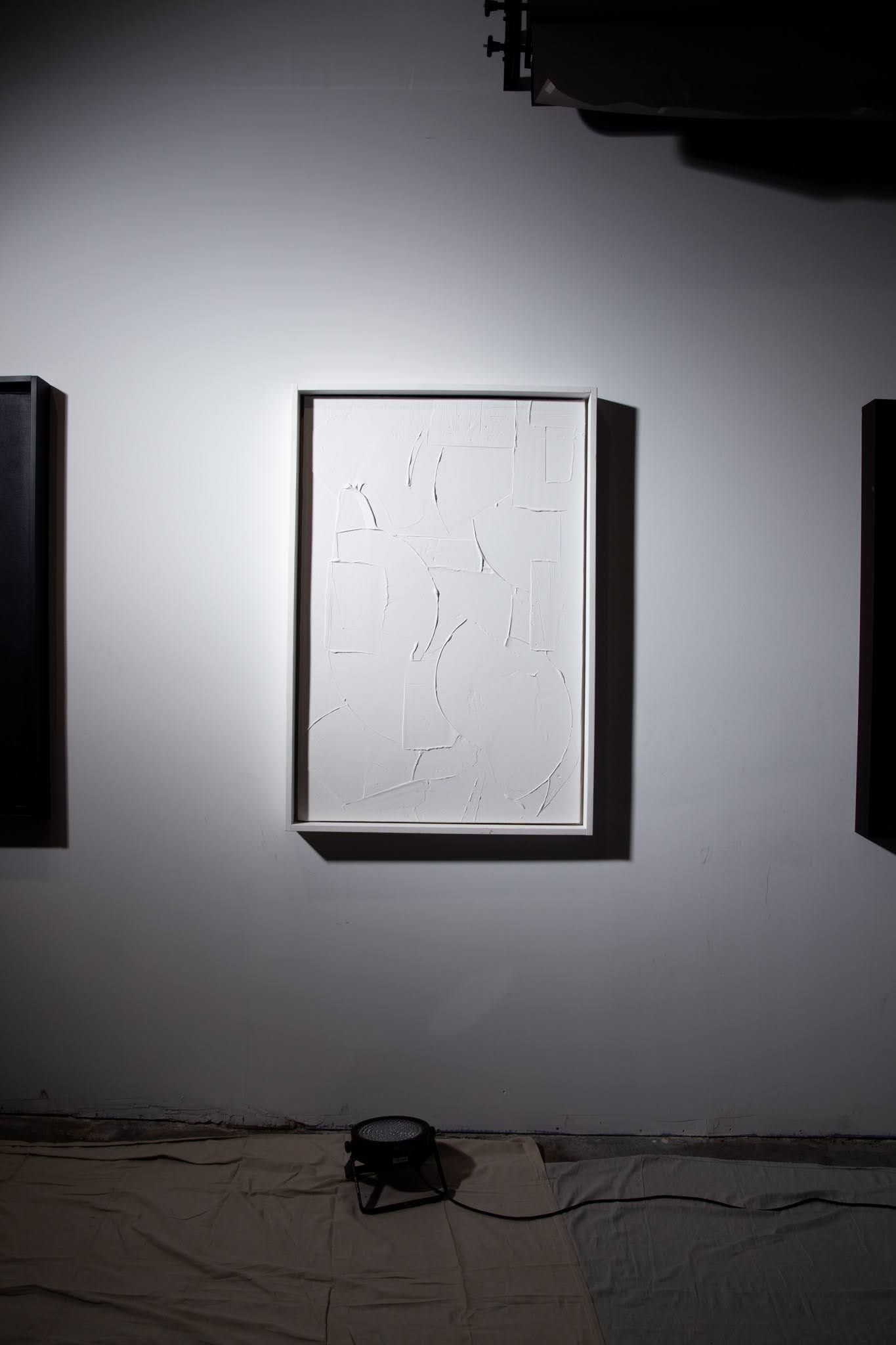 White framed artwork with sparse black dots on a white wall; lit by a spotlight; art by Matt Remsbecher. 