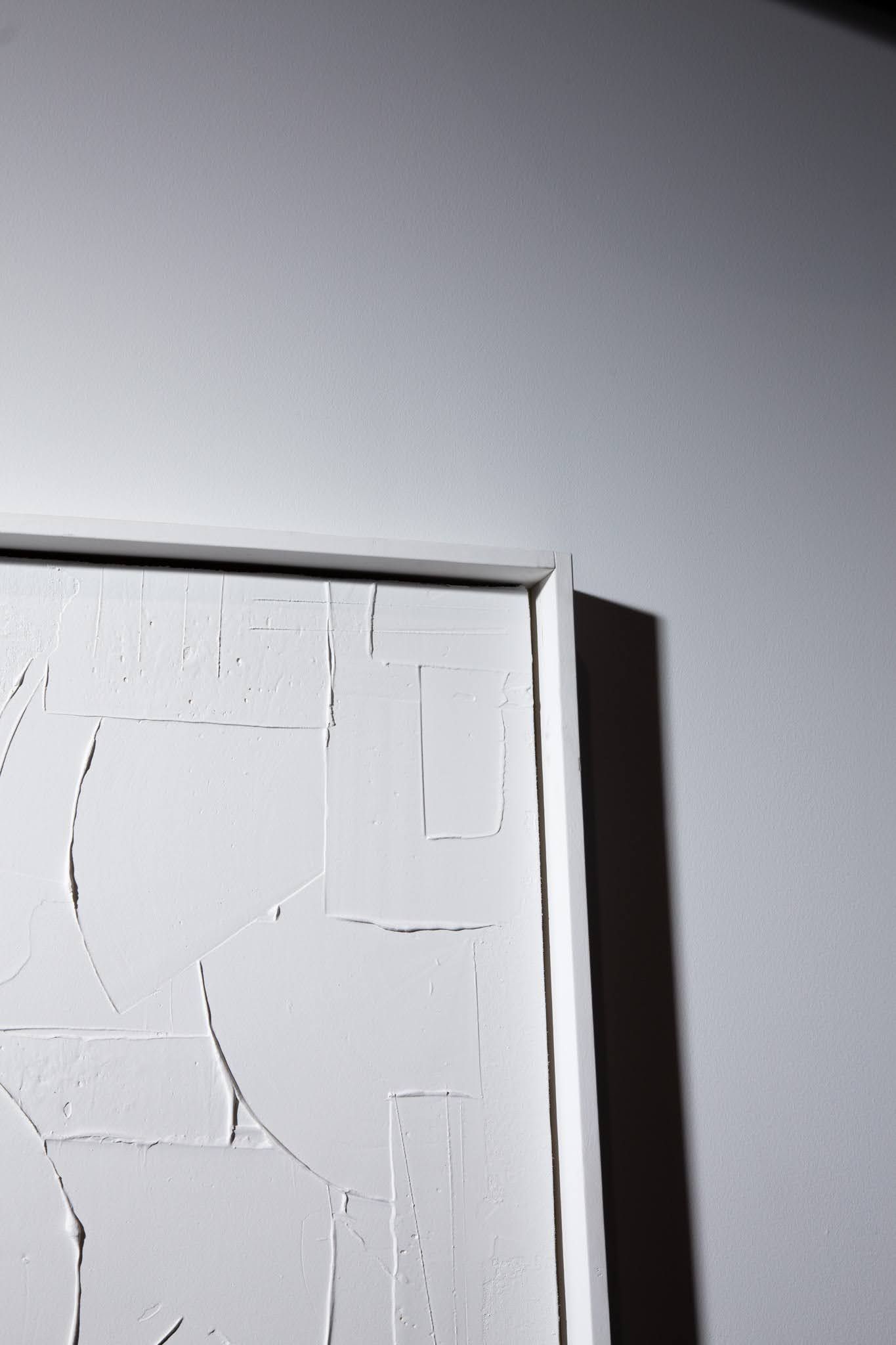 White textured artwork in a white frame, against a white wall; art by Matt Remsbecher. 