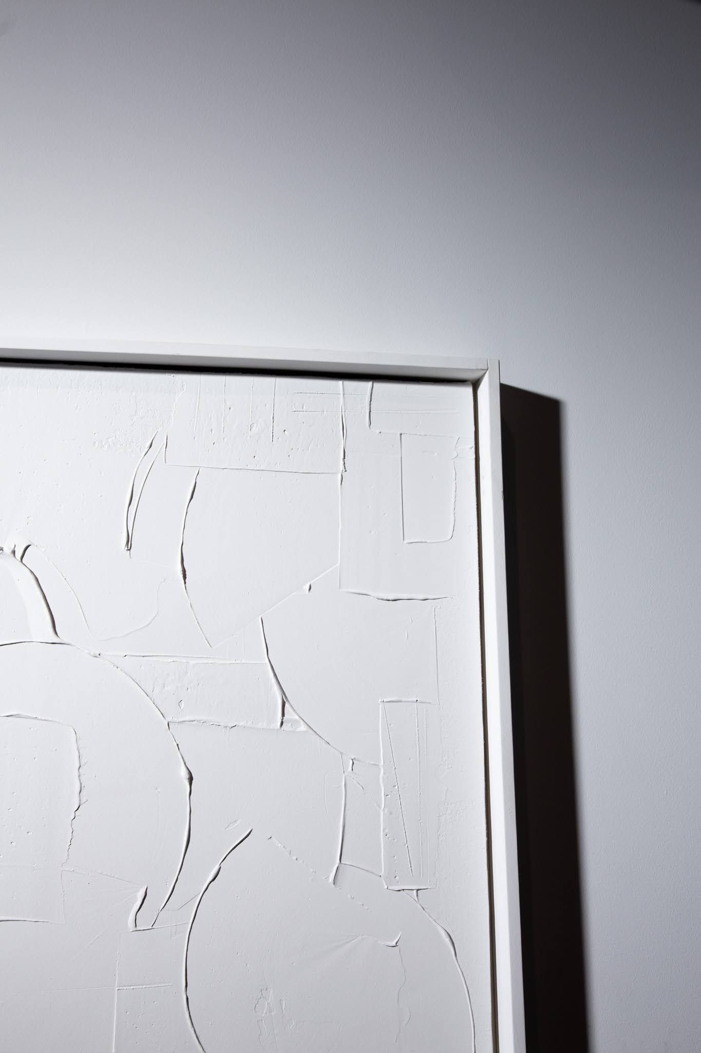 Corner view of a white, textured abstract artwork with a visible frame, against a white wall; art by Matt Remsbecher. 