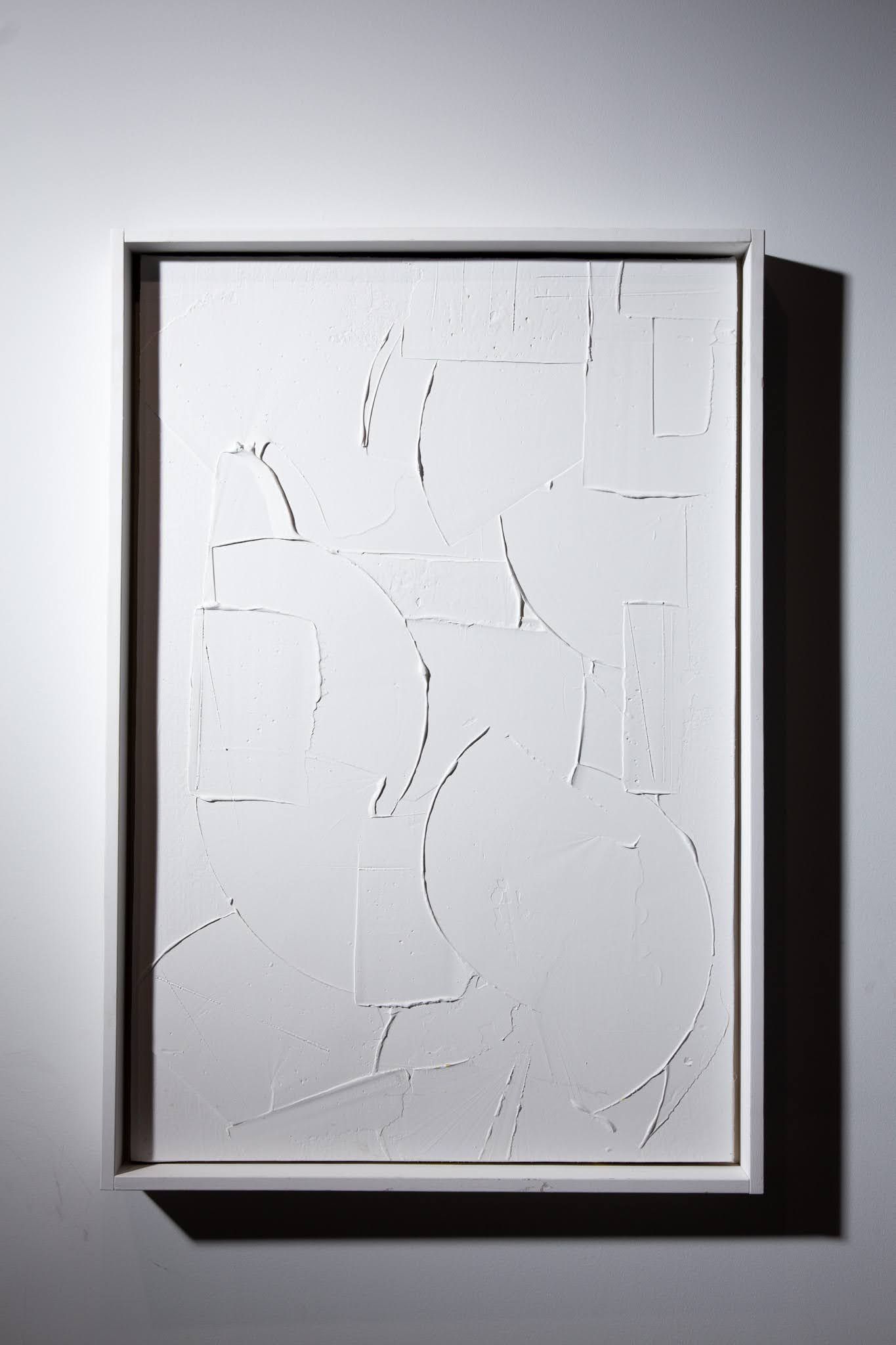 White abstract artwork in a white frame on a white wall. The artwork has cut-out lines and shapes; art by Matt Remsbecher. 