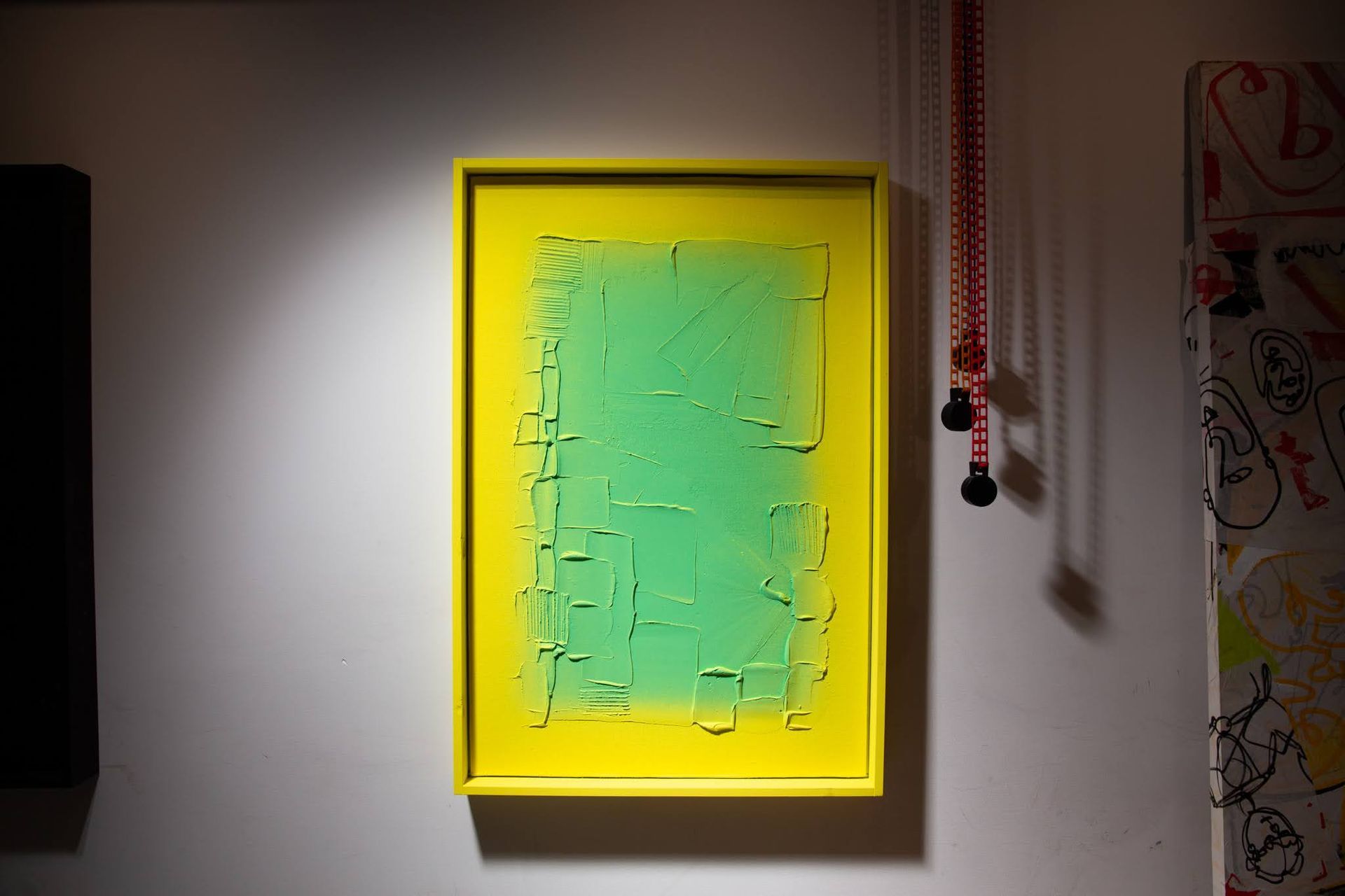 Green abstract painting in a yellow frame on a white wall. Red beaded string hangs nearby; art by Matt Remsbecher. 