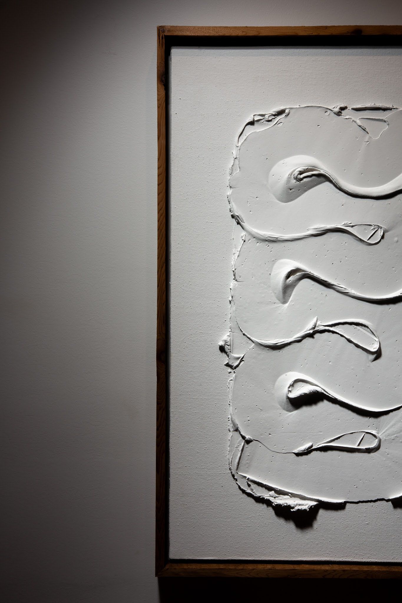 Close-up of a white textured abstract art piece with a swirling pattern in a dark wood frame; art by Matt Remsbecher. 