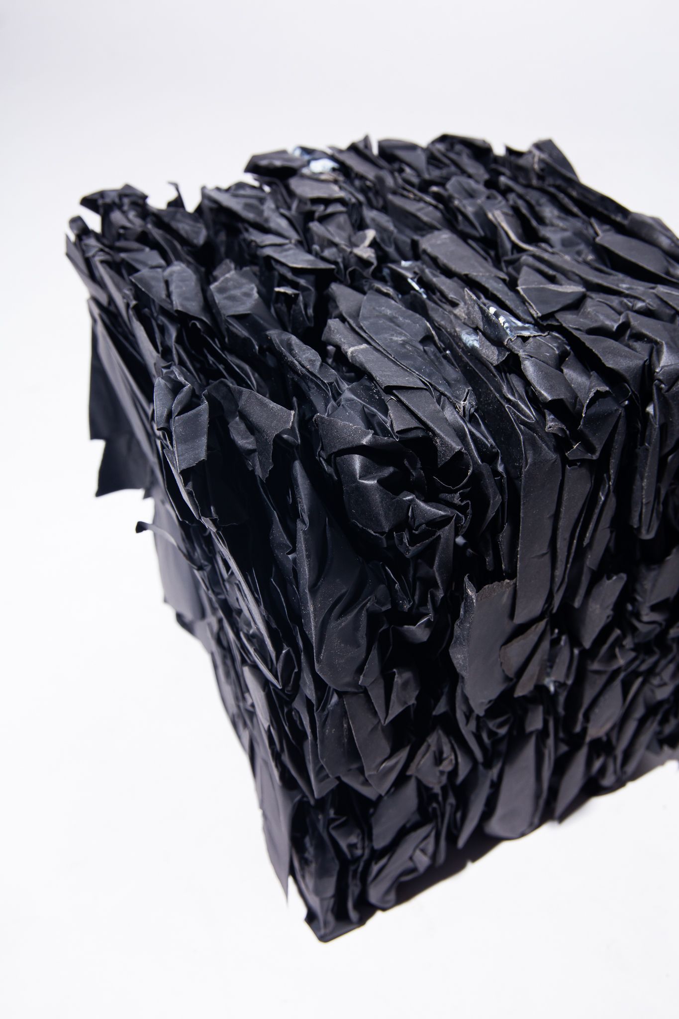 A cube-shaped block constructed from layered, torn black plastic on a white background; art by Matt Remsbecher. 