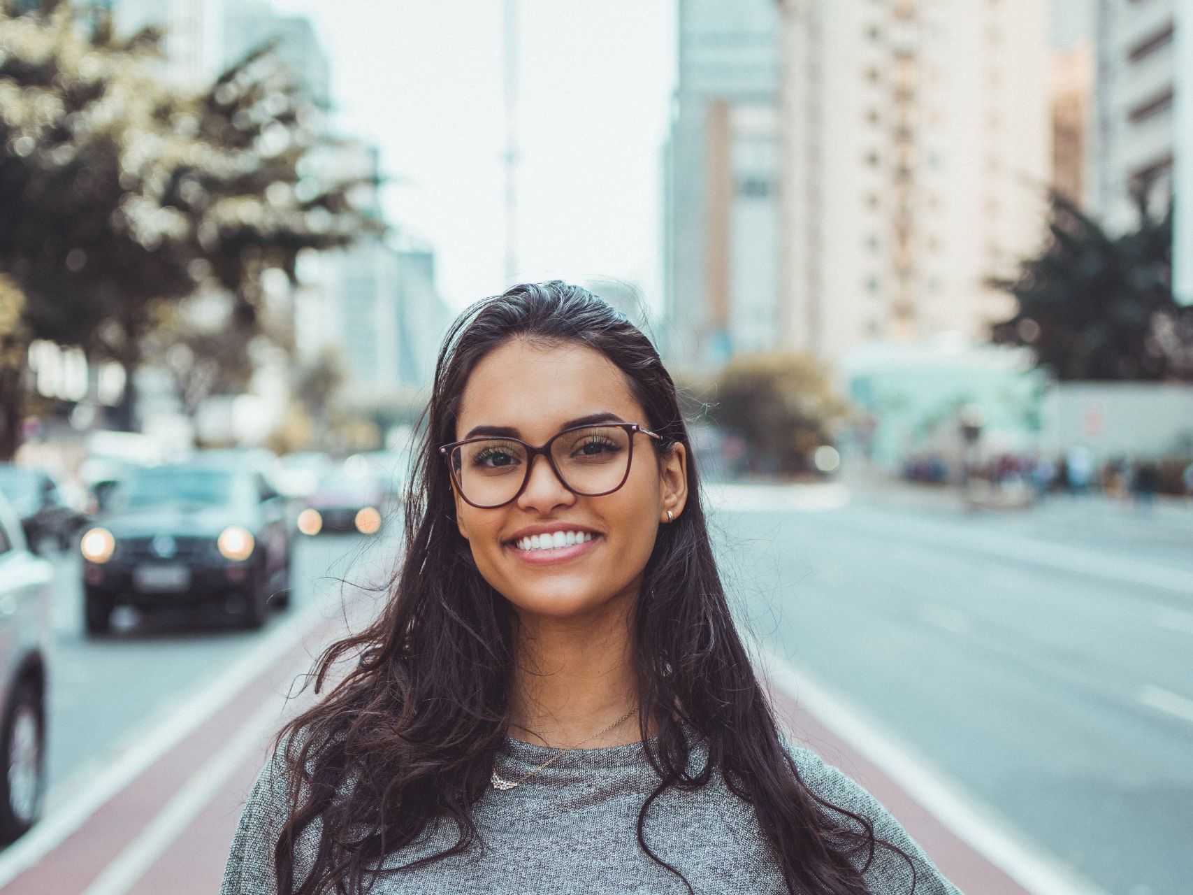 A woman wearing glasses is smiling in front of a city street.