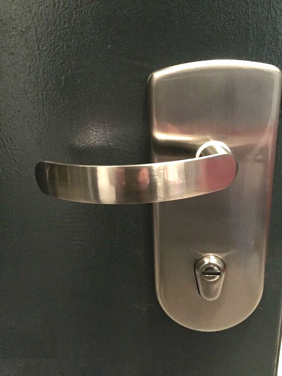 תקריב של ידית דלת מעוצבת  כסופה בעיצוב מודרני המותקנת על פלטת מתכת תואמת עם חור למפתח מתחתיה על רקע דלת כהה