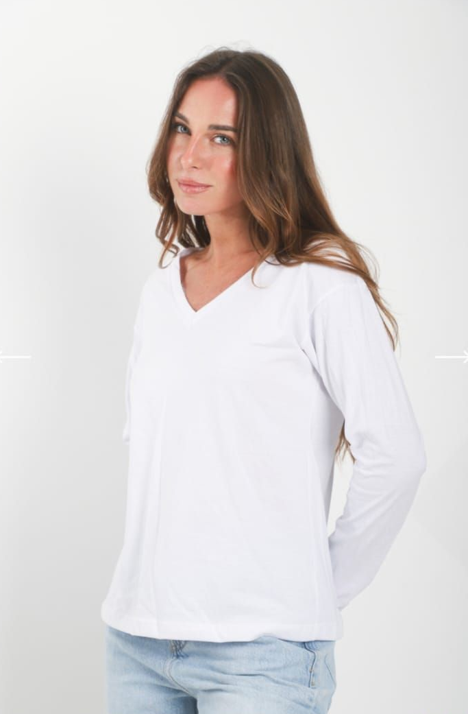 Mujer con una blusa blanca de cuello en V y vaqueros azul claro, de pie sobre un fondo claro liso.