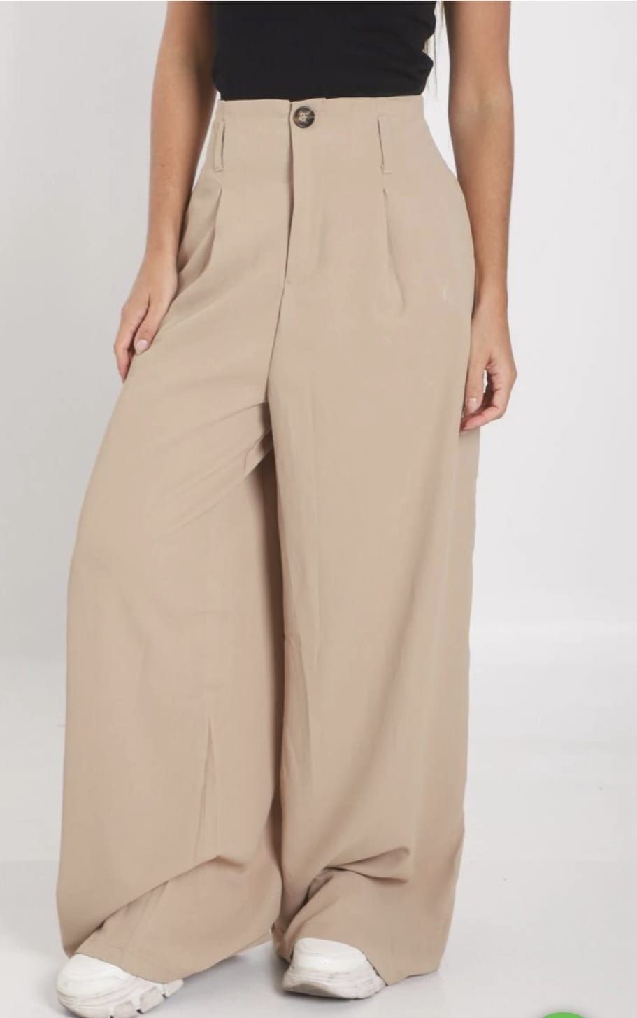 Pantalones anchos color beige con pliegues en la parte delantera y zapatillas blancas en una modelo sobre un fondo liso.