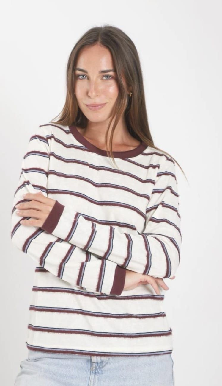 Mujer con un suéter blanco de rayas, con los brazos cruzados, de pie sobre un fondo claro.