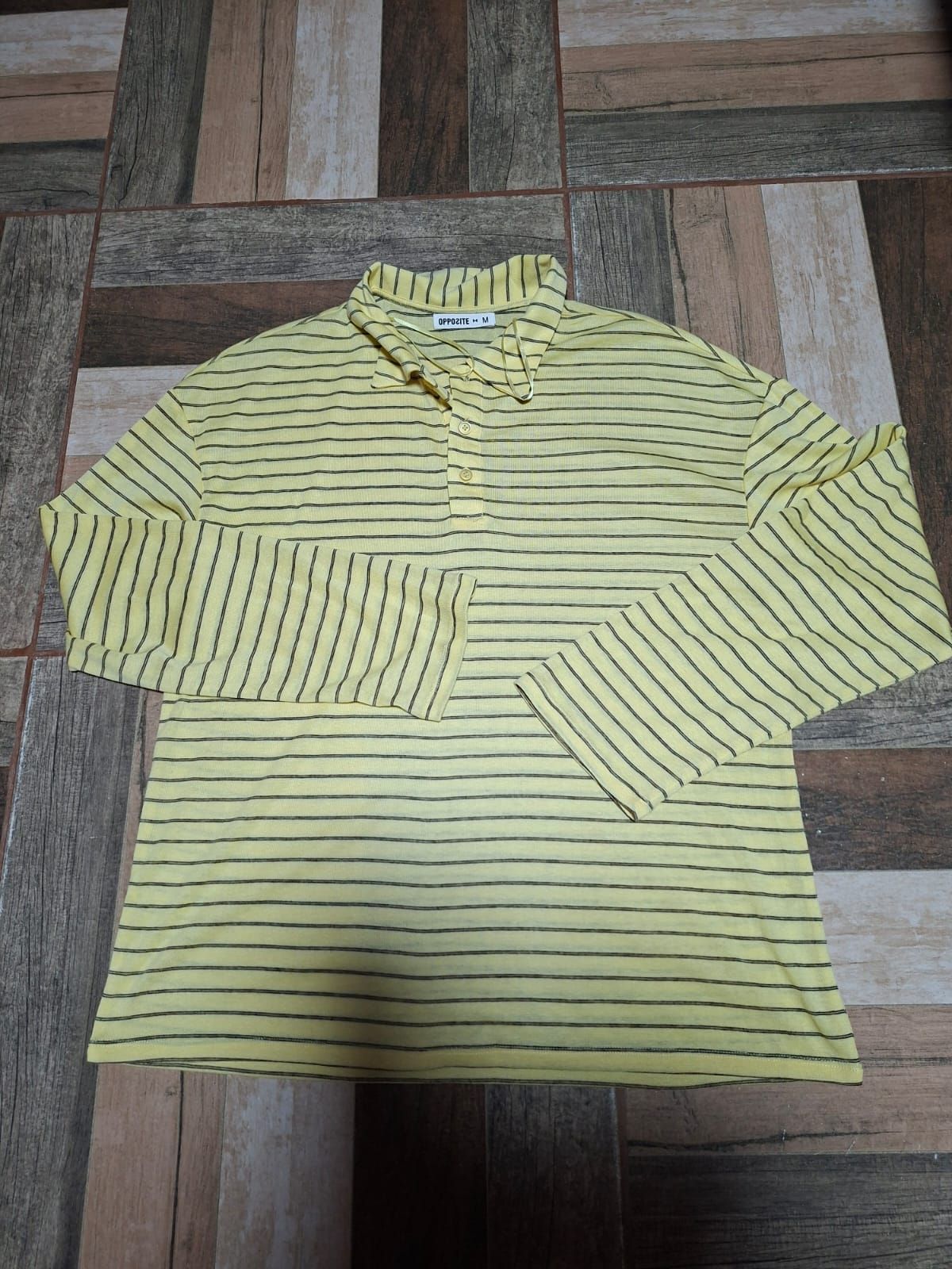 Camisa de manga larga a rayas granates y blancas extendida sobre un suelo de madera.