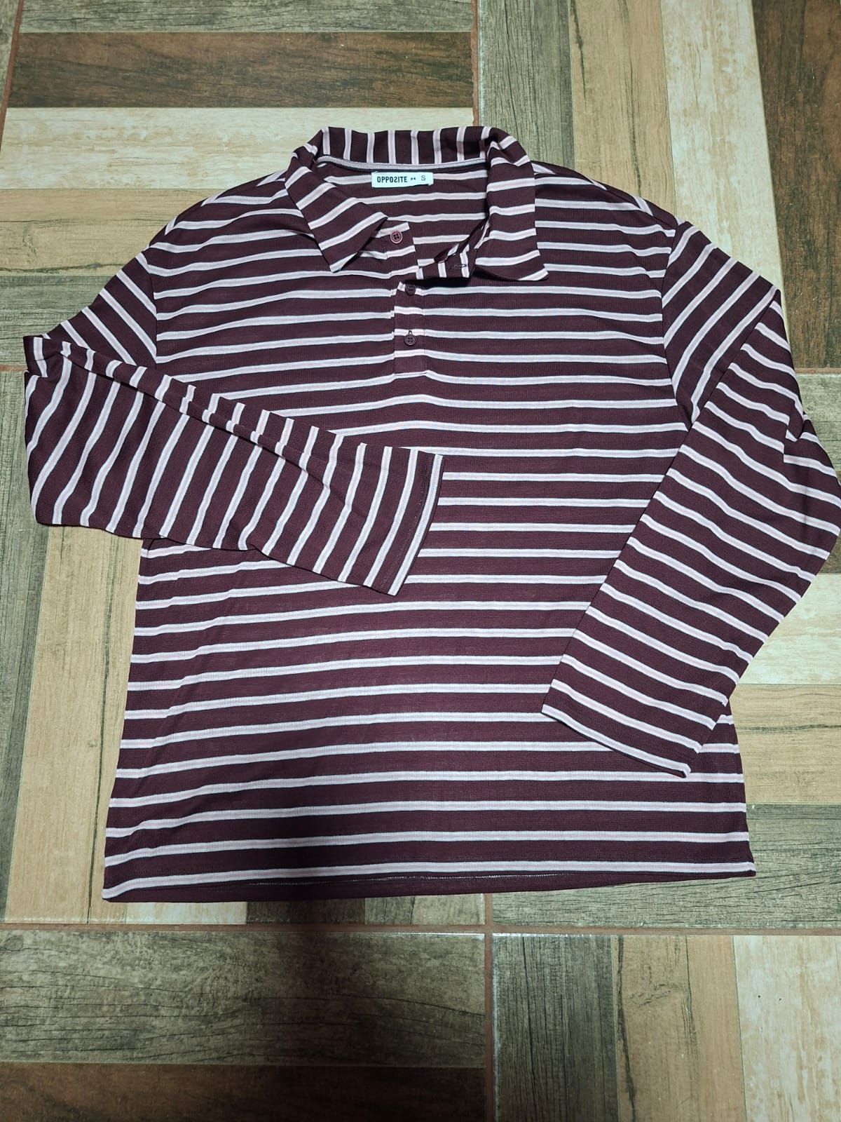 Camisa de manga larga a rayas granates y blancas extendida sobre un suelo de madera.