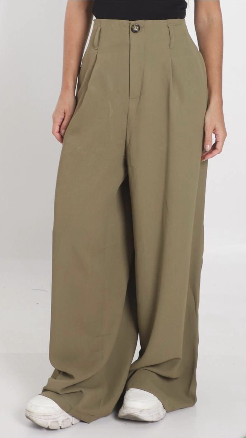 Persona con pantalones anchos de color caqui y zapatillas blancas, de pie sobre un fondo liso.