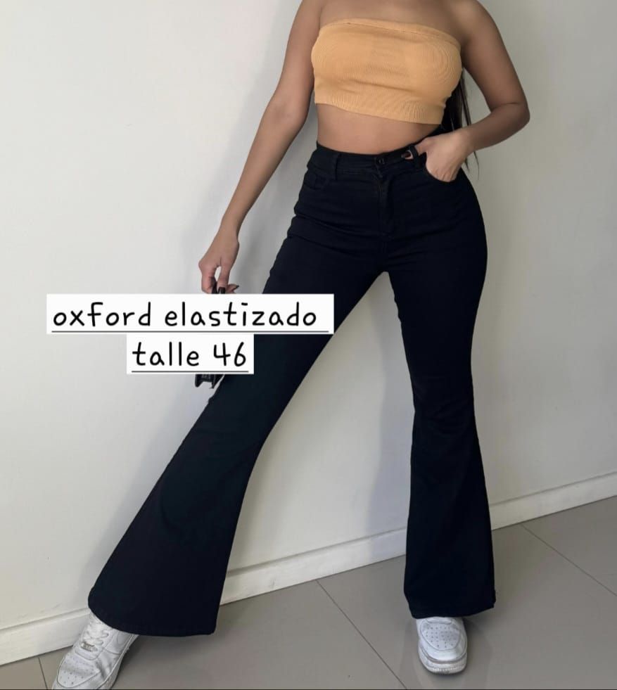 Mujer con top beige y pantalón oxford negro, de pie en interior; texto: “oxford elastizado talle 46”