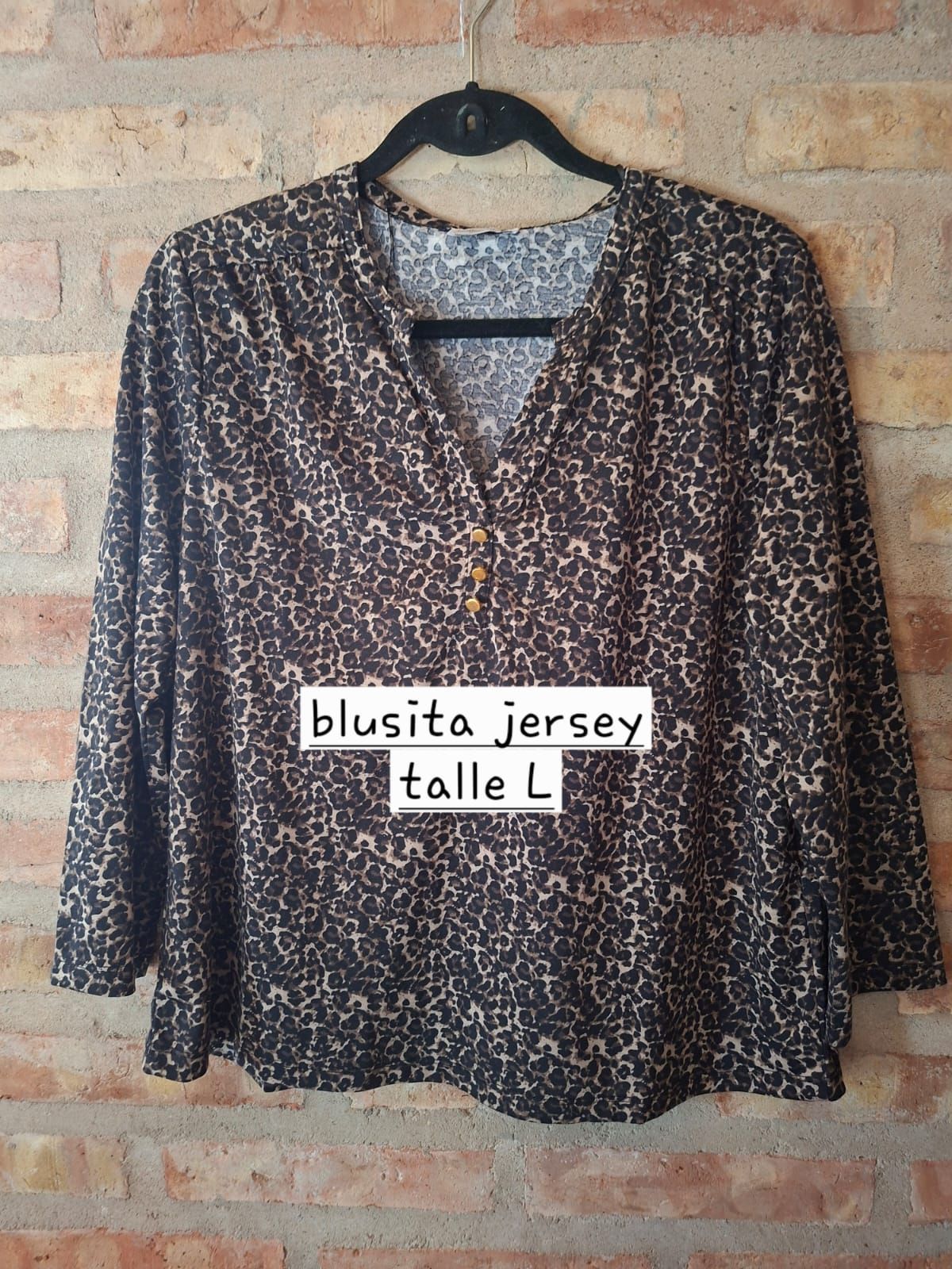 Blusa granate con estampado floral colgada en una percha contra una pared de ladrillos.