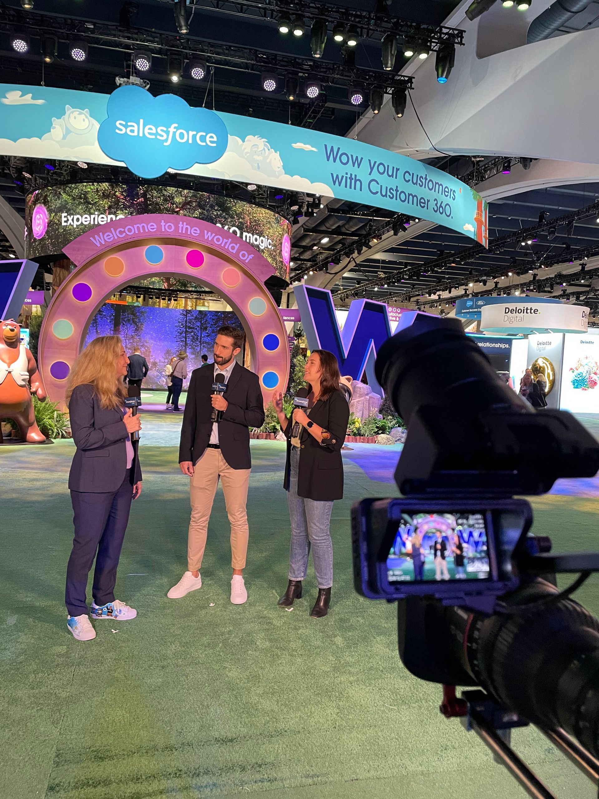 Three people being interviewed in front of a Salesforce display with a camera focused on them.