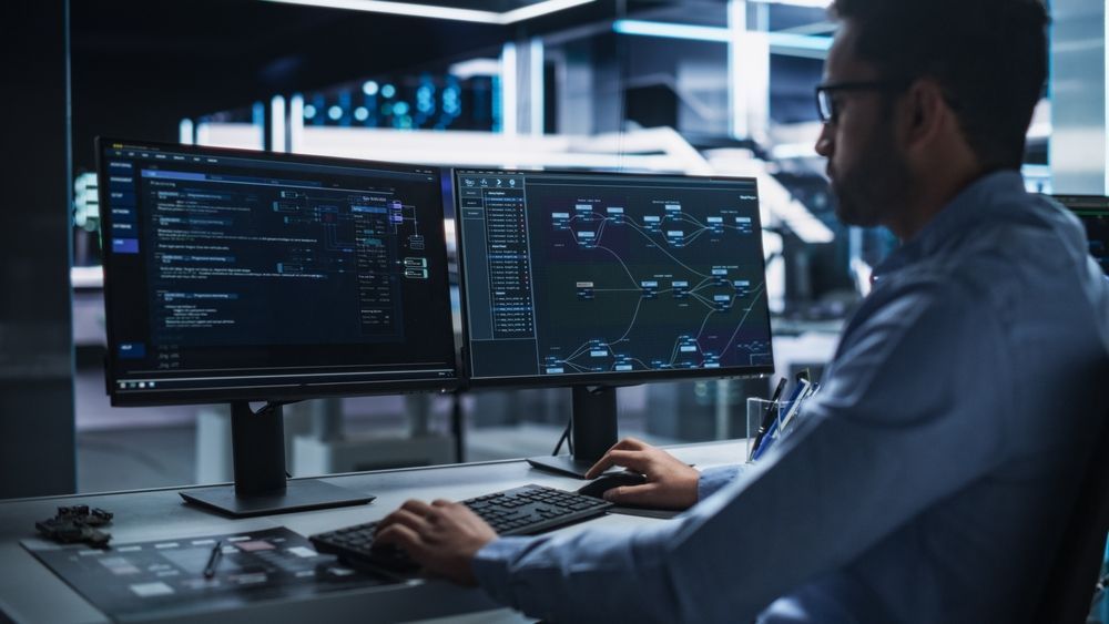 Person Working at Dual Monitors in a Dimly Lit Office — Compago Technologies In Cambridge, TAS