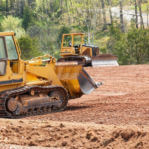 Two bulldozers are working on a dirt field.