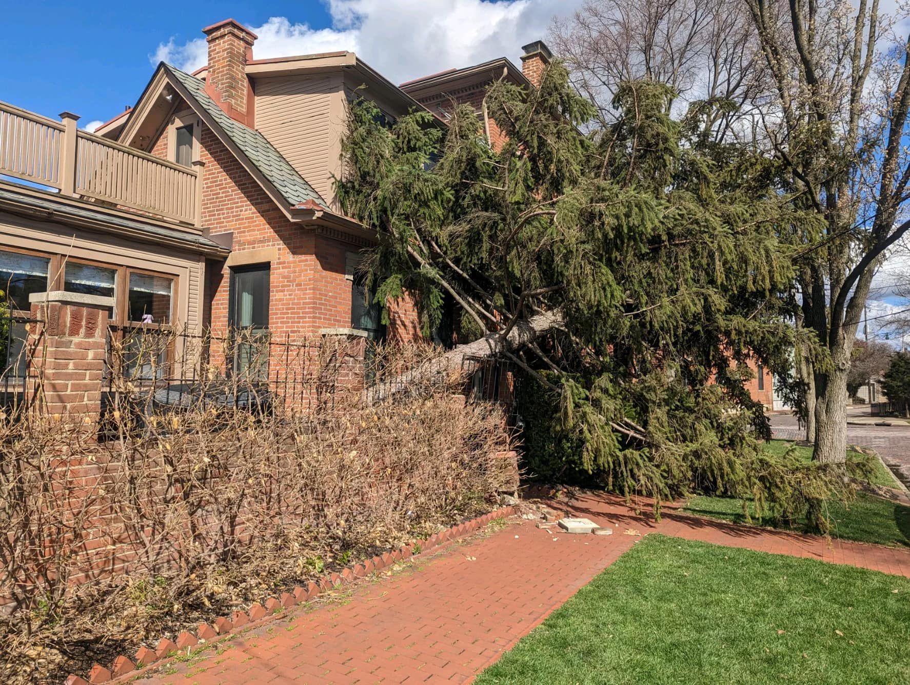 A large brick house with a fallen tree in front of it.