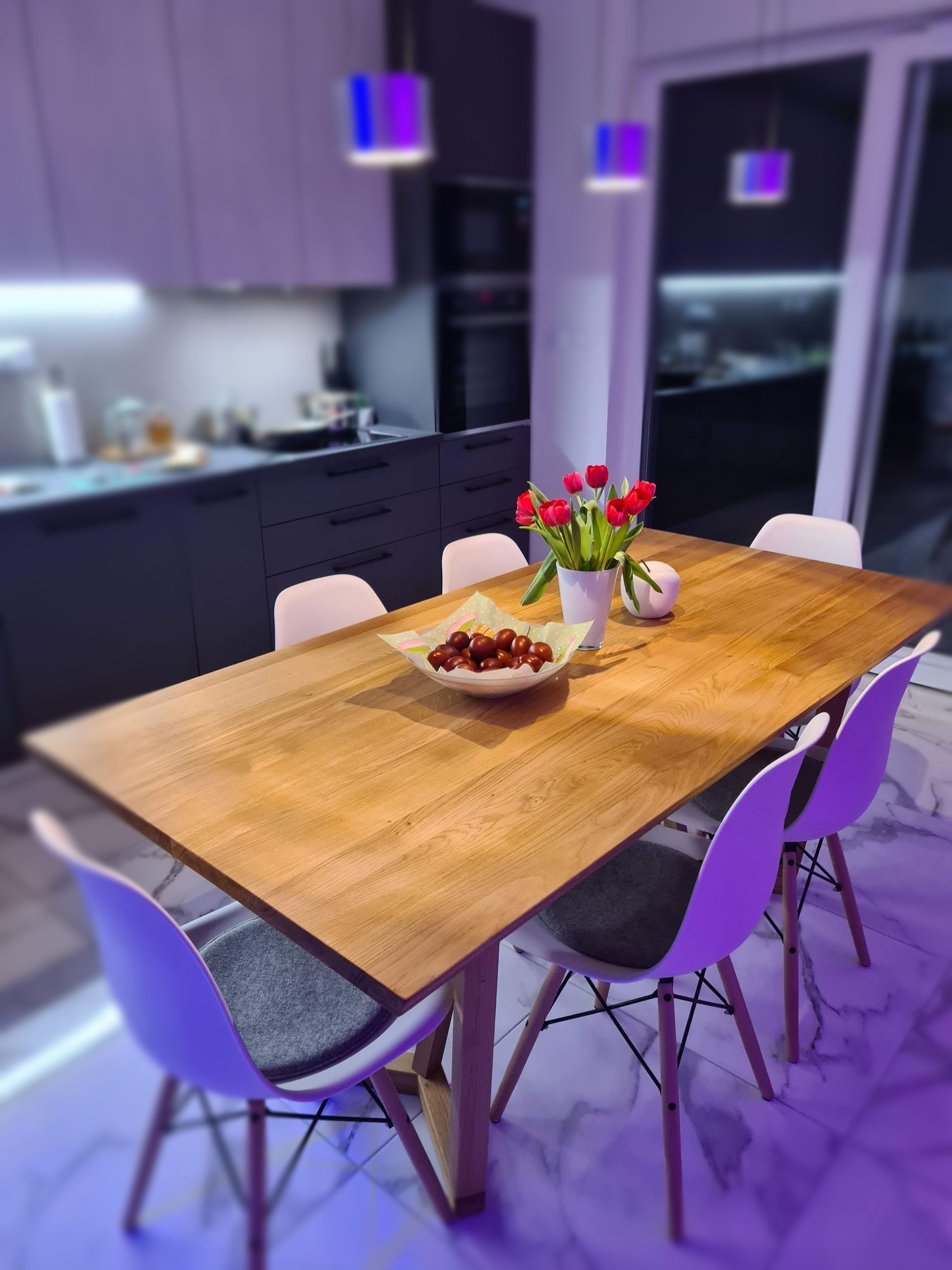 Wooden kitchen table with red tulips, bowl of cherries, surrounded by white chairs.