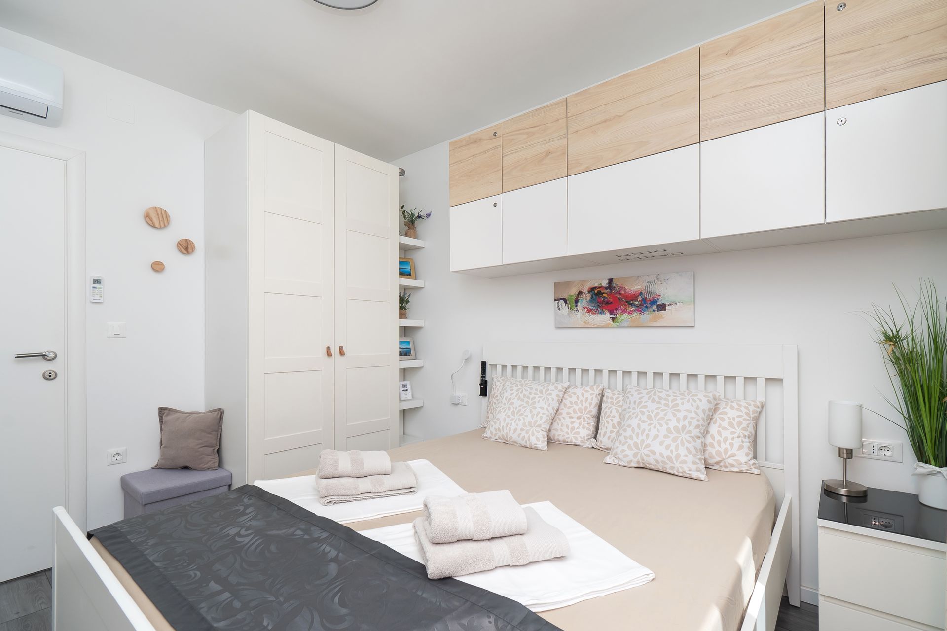 Bedroom with white walls, bed, and cabinets; a neutral color scheme with wood accents.