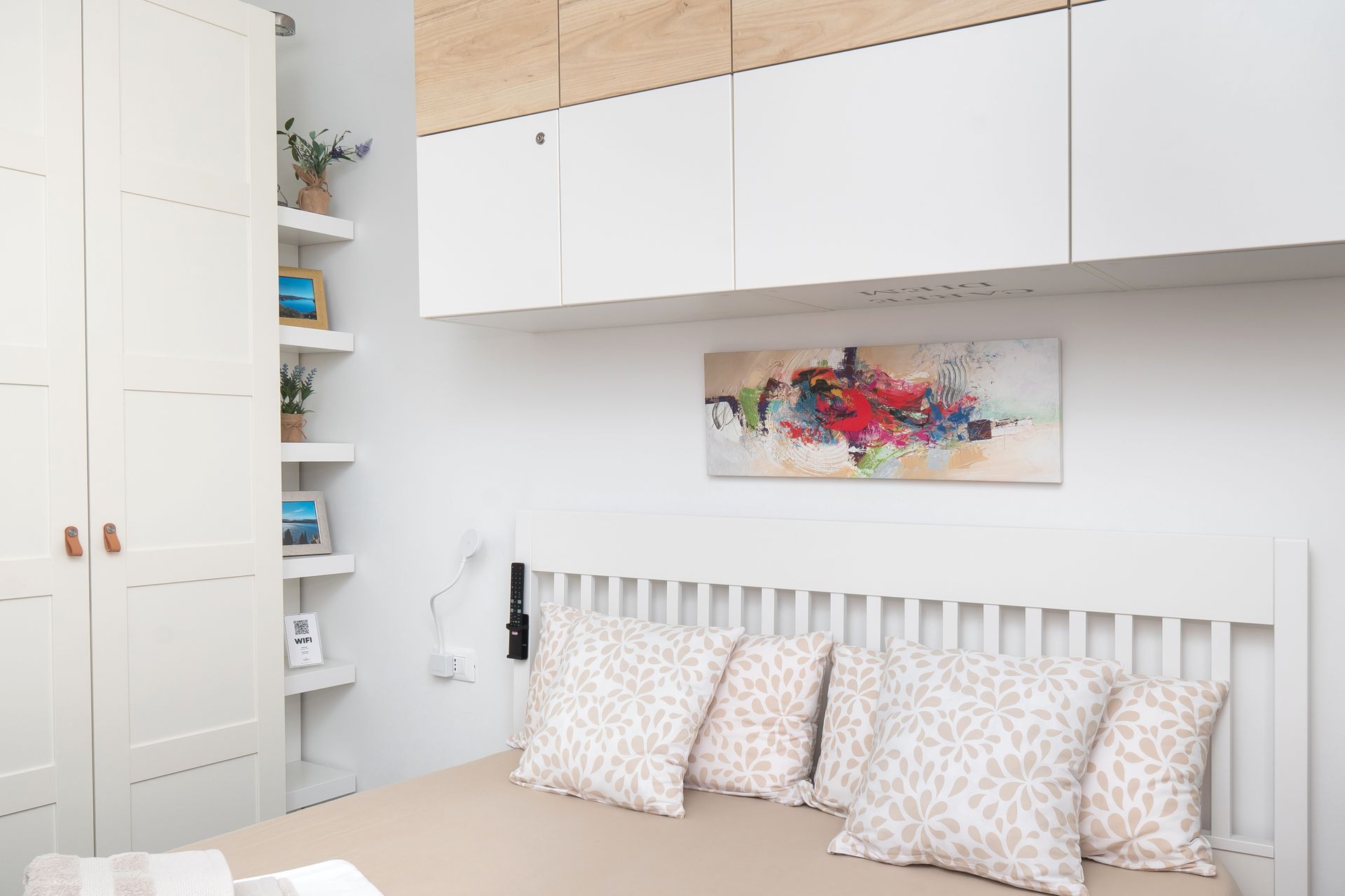 Bedroom with white furniture, artwork, and patterned pillows.