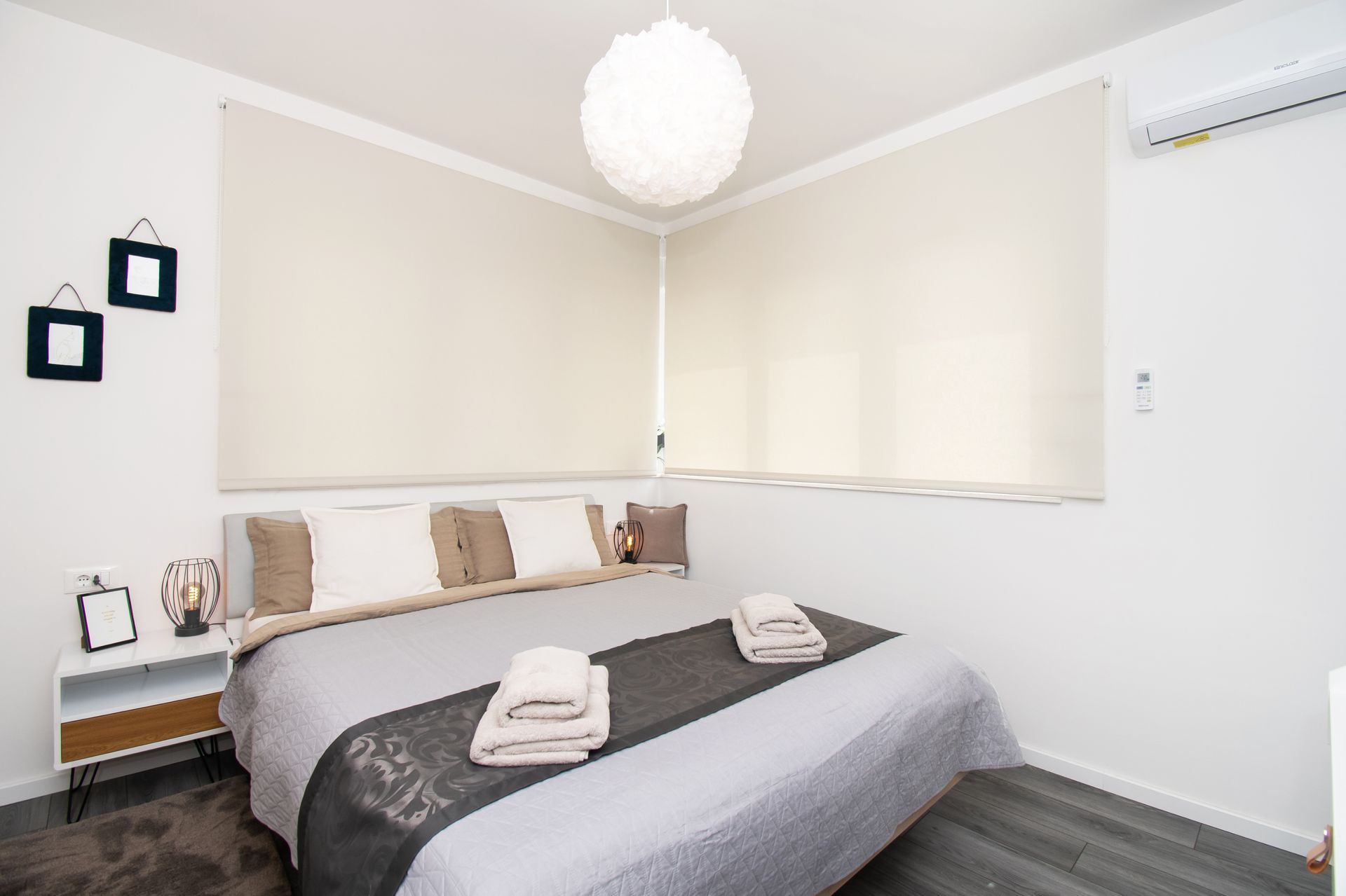 Bedroom with a bed, two windows with blinds, a nightstand, and a decorative light fixture.