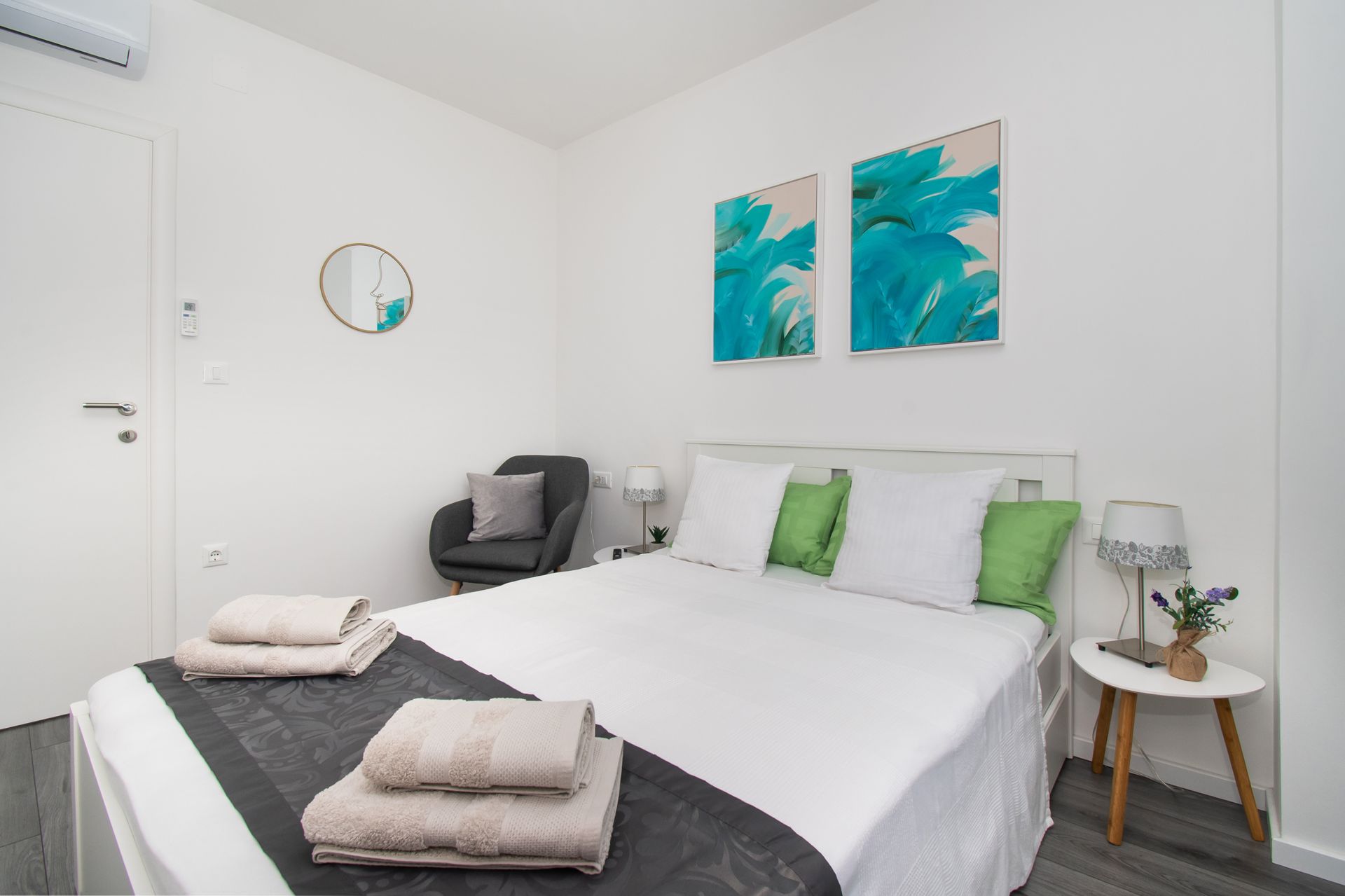 White bedroom with a bed, gray chair, and turquoise artwork.