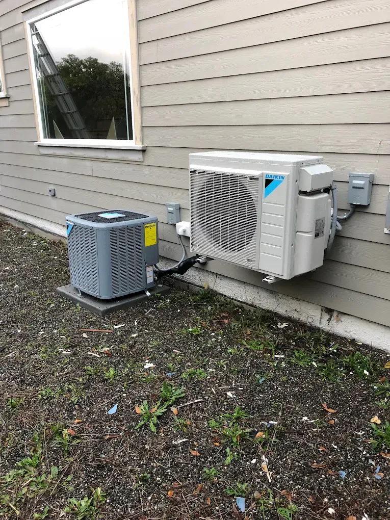Air conditioning units mounted on a building's exterior. One is square, the other is rectangular and wall-mounted.