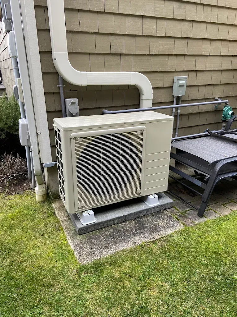 Exterior heat pump unit next to a house with metal ventilation.