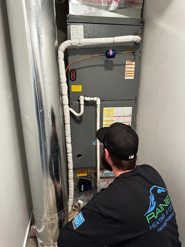 HVAC technician inspecting a furnace in a utility room. He is wearing a black shirt.