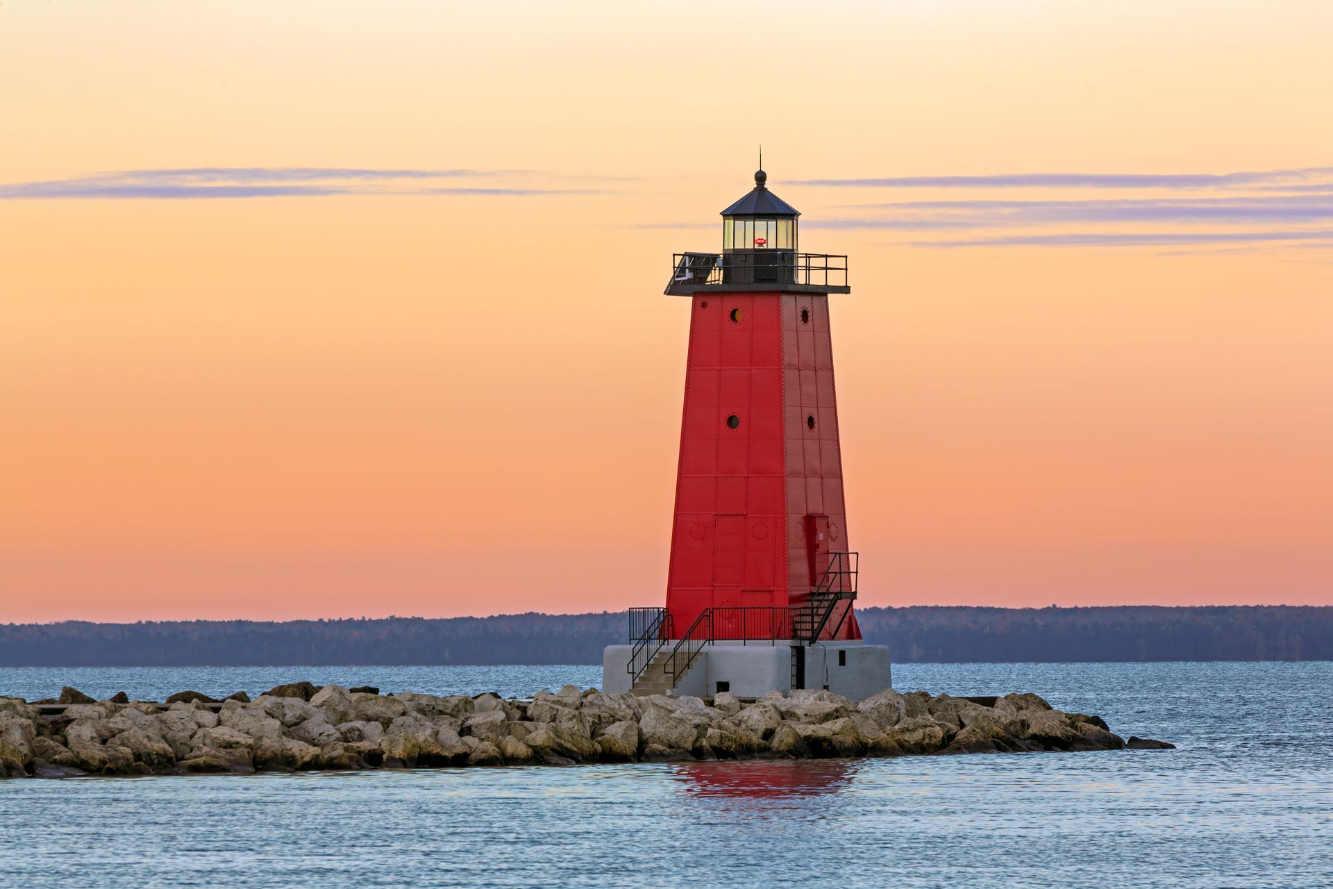a red lighthouse is sitting on top of a small island in the middle of the ocean .