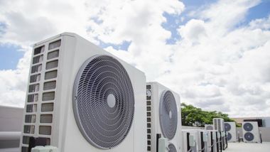 Row of white outdoor air conditioning units with large fans on a rooftop under a cloudy sky