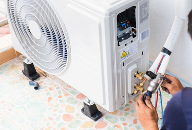 Technician repairing outdoor air conditioner unit with tools and wires attached