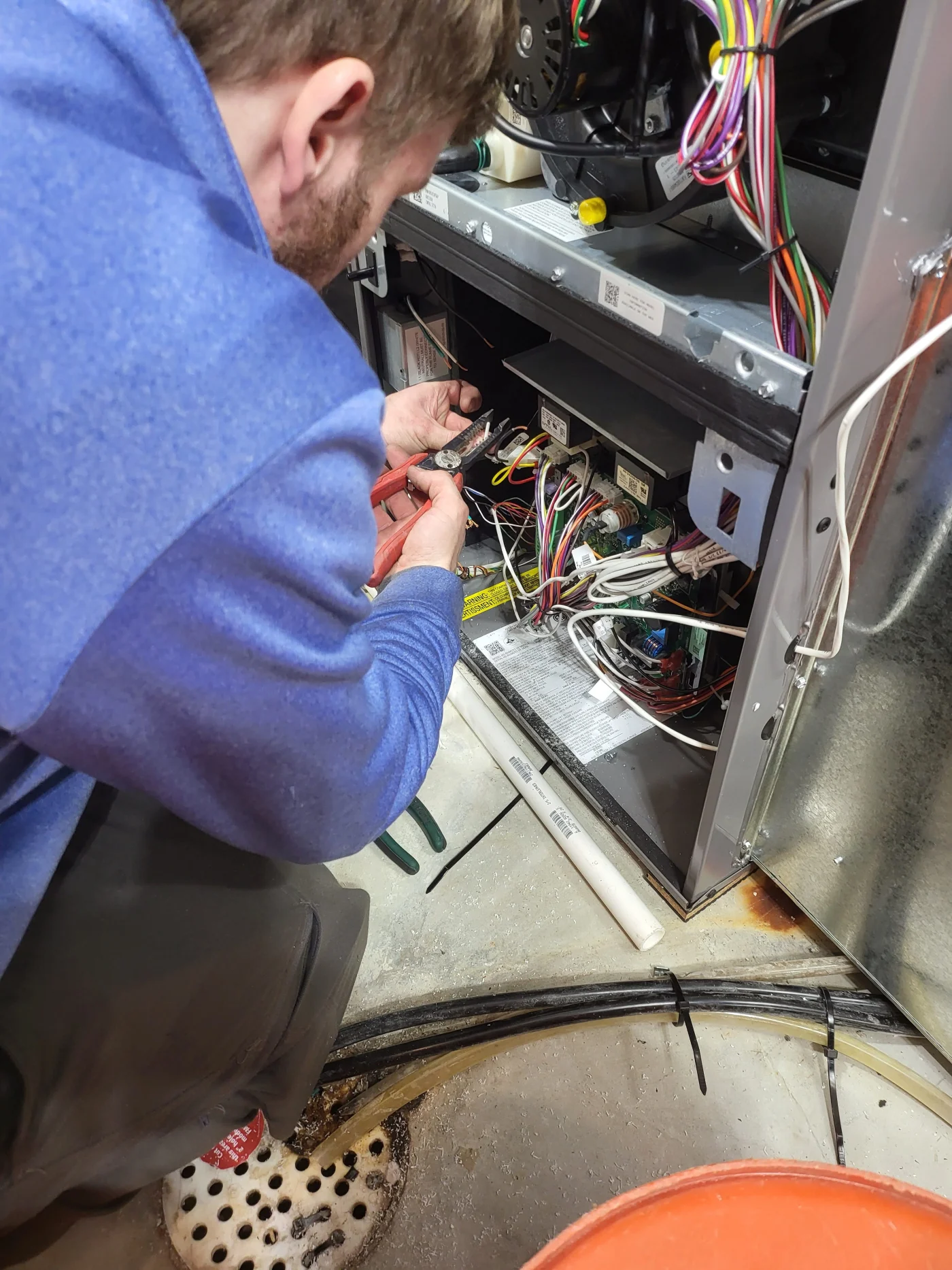 Technician in blue shirt wiring inside an open electrical panel with exposed cables