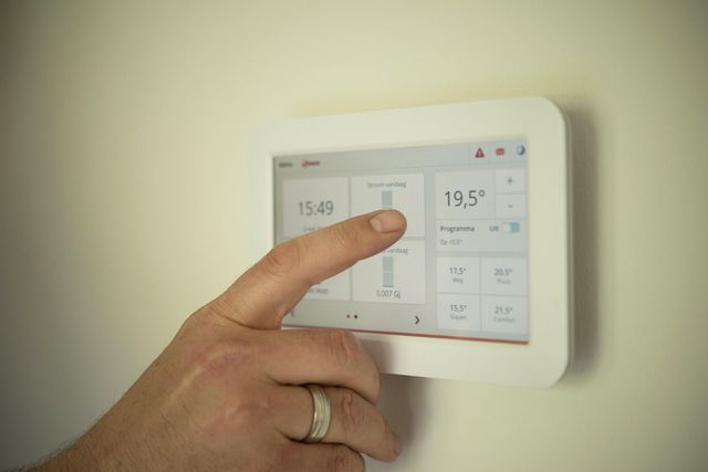 Hand pressing a white touchscreen thermostat on a wall