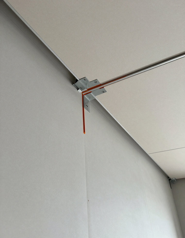 Angolo del soffitto con un tubo metallico, un morsetto e un cavo rosso che pendono lungo una parete bianca.