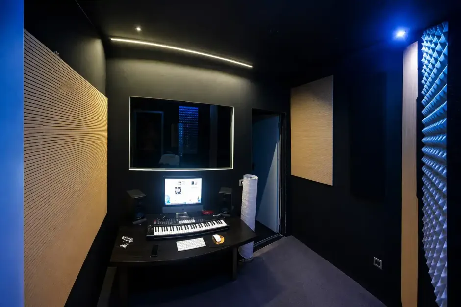 Studio di registrazione buio con pareti insonorizzate, mixer e monitor luminoso sotto luci d'accento blu.