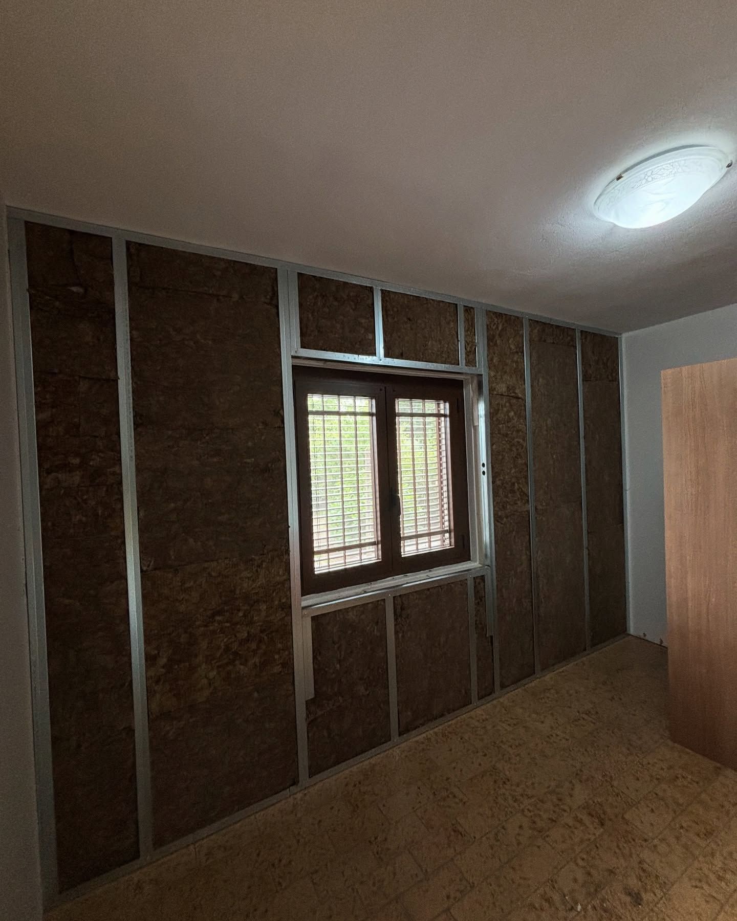 Stanza vuota e non rifinita con struttura a vista, una finestra e una lampada a soffitto.