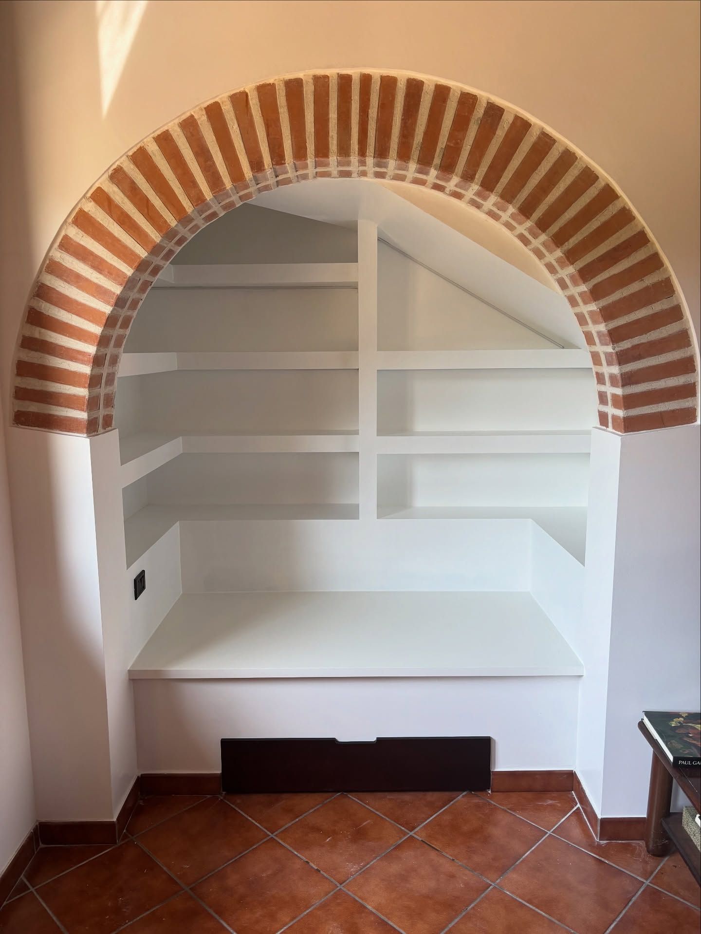 Mensola a nicchia bianca integrata, incorniciata da un arco in mattoni rossi sopra un pavimento in piastrelle di terracotta.