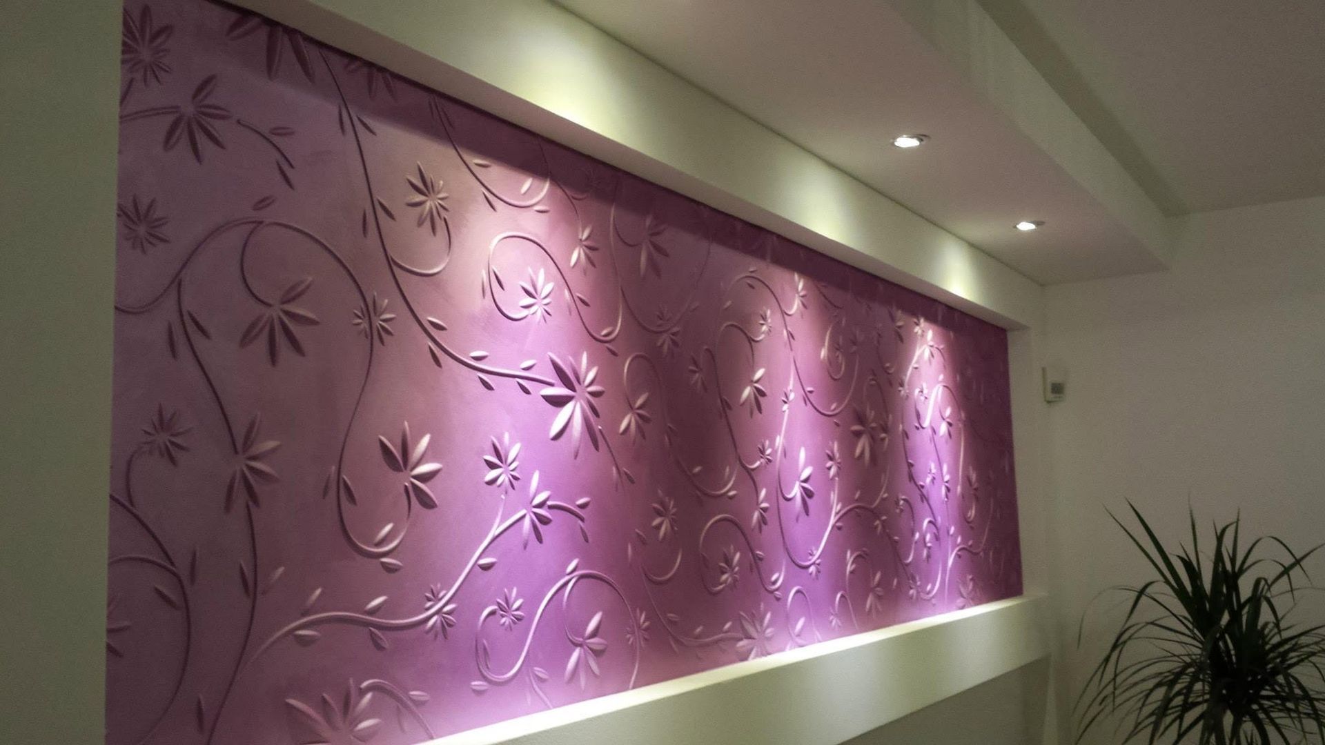 Pannello murale viola testurizzato con motivi floreali e faretti a incasso a soffitto in un interno moderno.