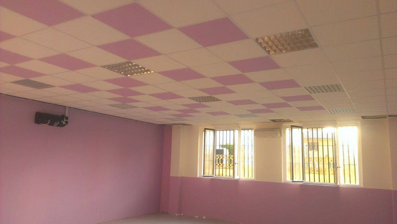 Stanza vuota con pareti rosa e soffitto a scacchiera, illuminata da finestre con sbarre gialle.