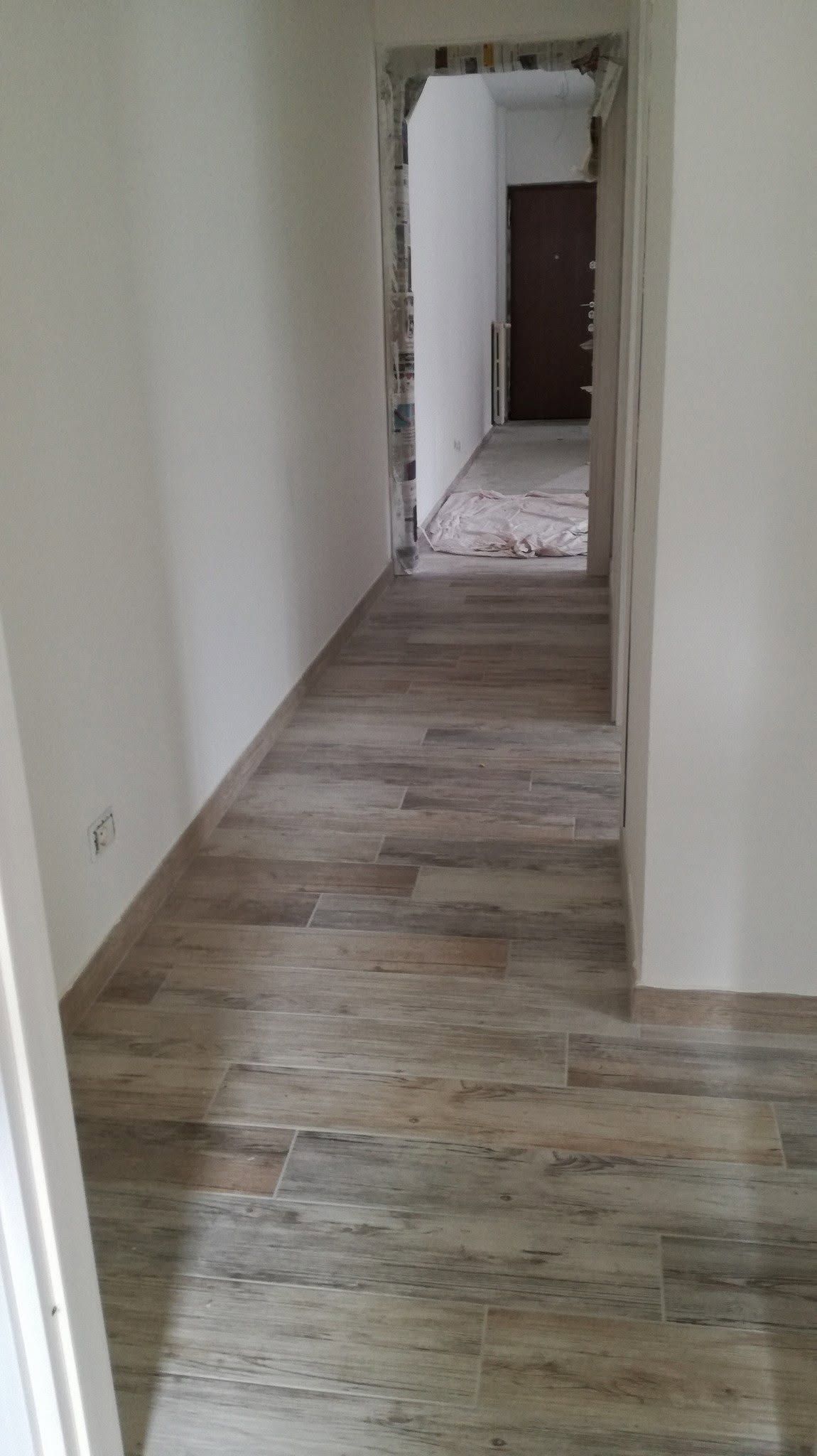 Stretto corridoio bianco con pavimento in legno grezzo e porte che conducono a una stanza più buia.