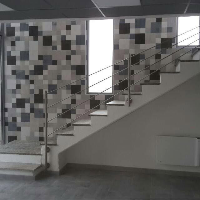 Scala moderna con ringhiera in acciaio inox in un interno grigio, accanto a una parete rivestita di piastrelle a mosaico.